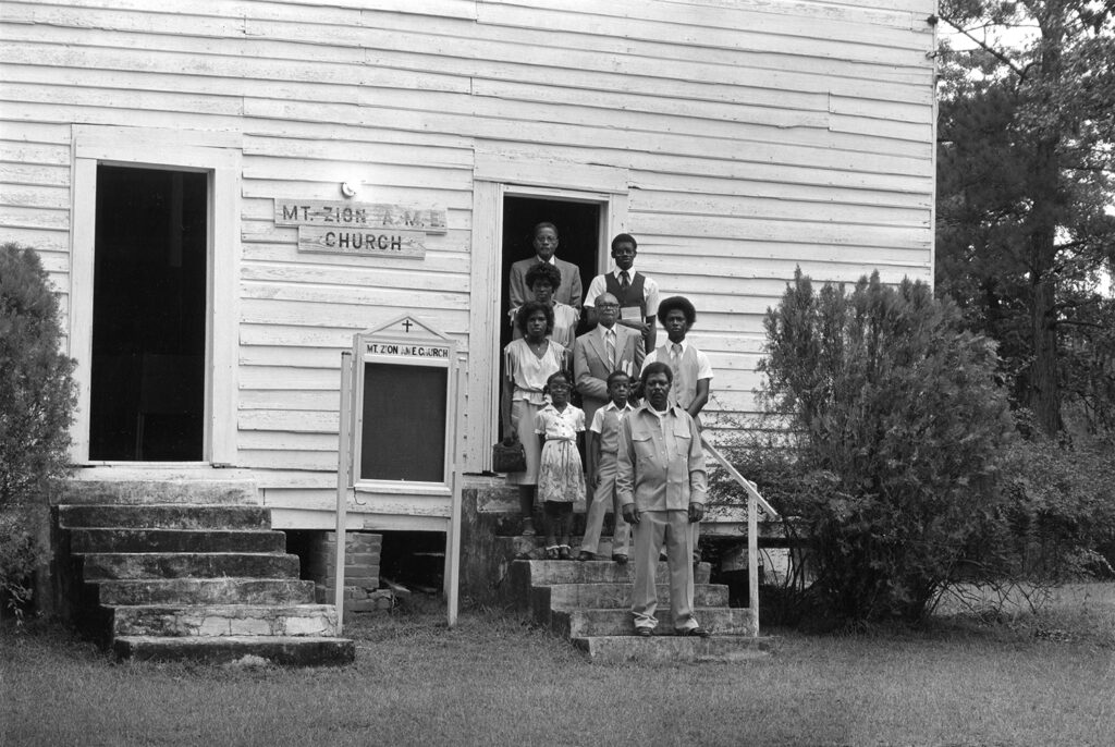 African-American church congregation stands of steps of wooden church building.
