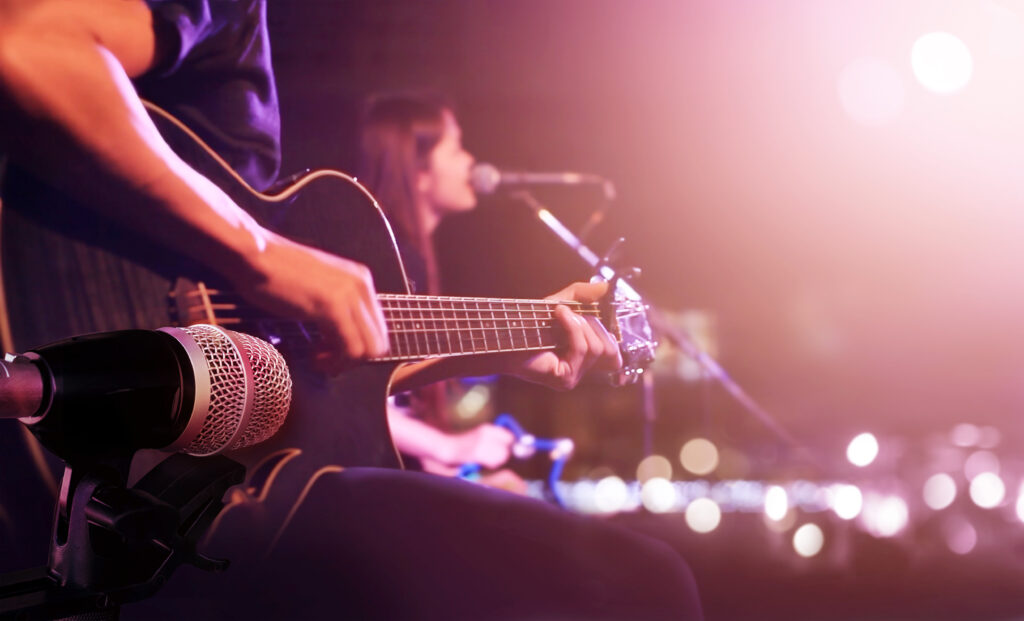 Hands playing guitar with woman singing into microphone in background