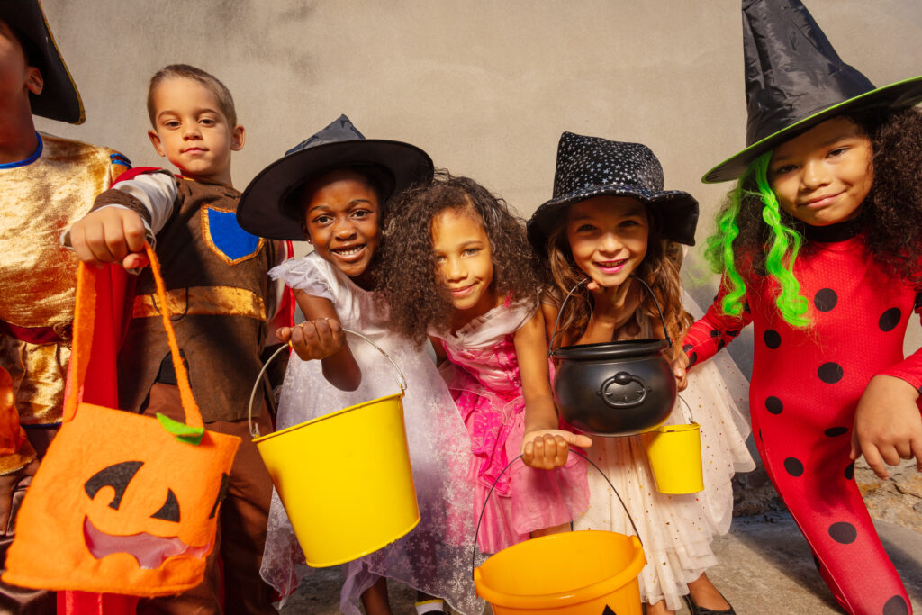 Many kids hold Halloween candy buckets and smile looking to the camera