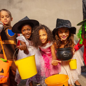 Many kids hold Halloween candy buckets and smile looking to the camera