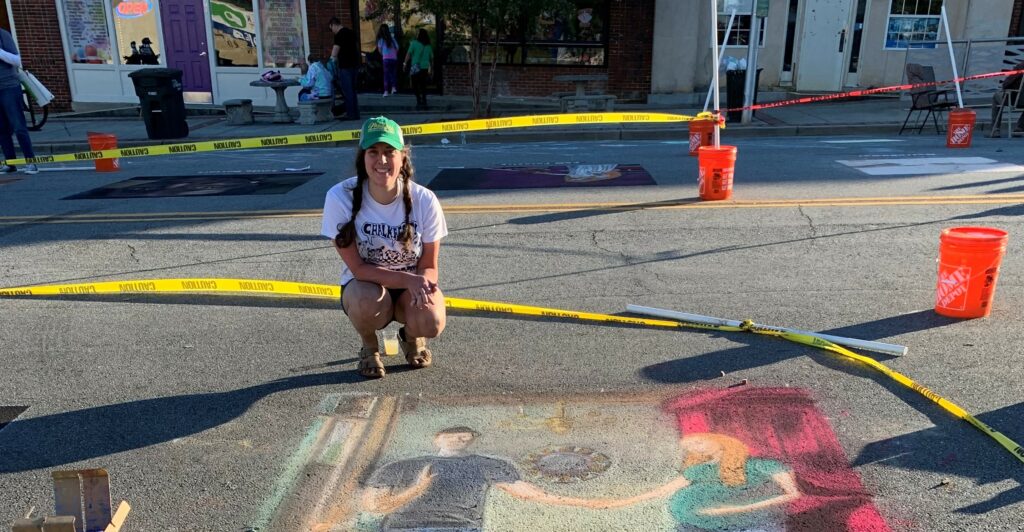 Artist poses with chalk art image of man and pregnant woman