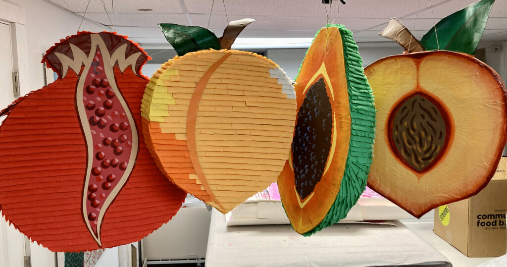 Four large hanging pinatas shaped like fruit