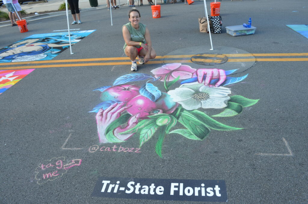 Artist poses with chalk art image of apples and magnolia blossoms