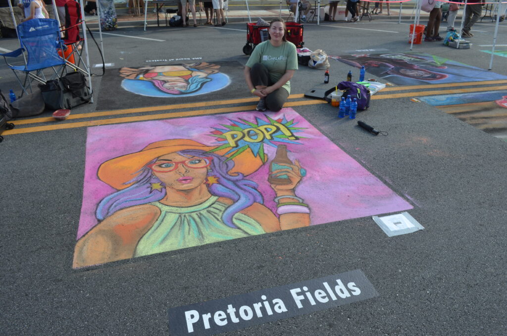 Artist poses with chalk image of woman with beverage and word pop