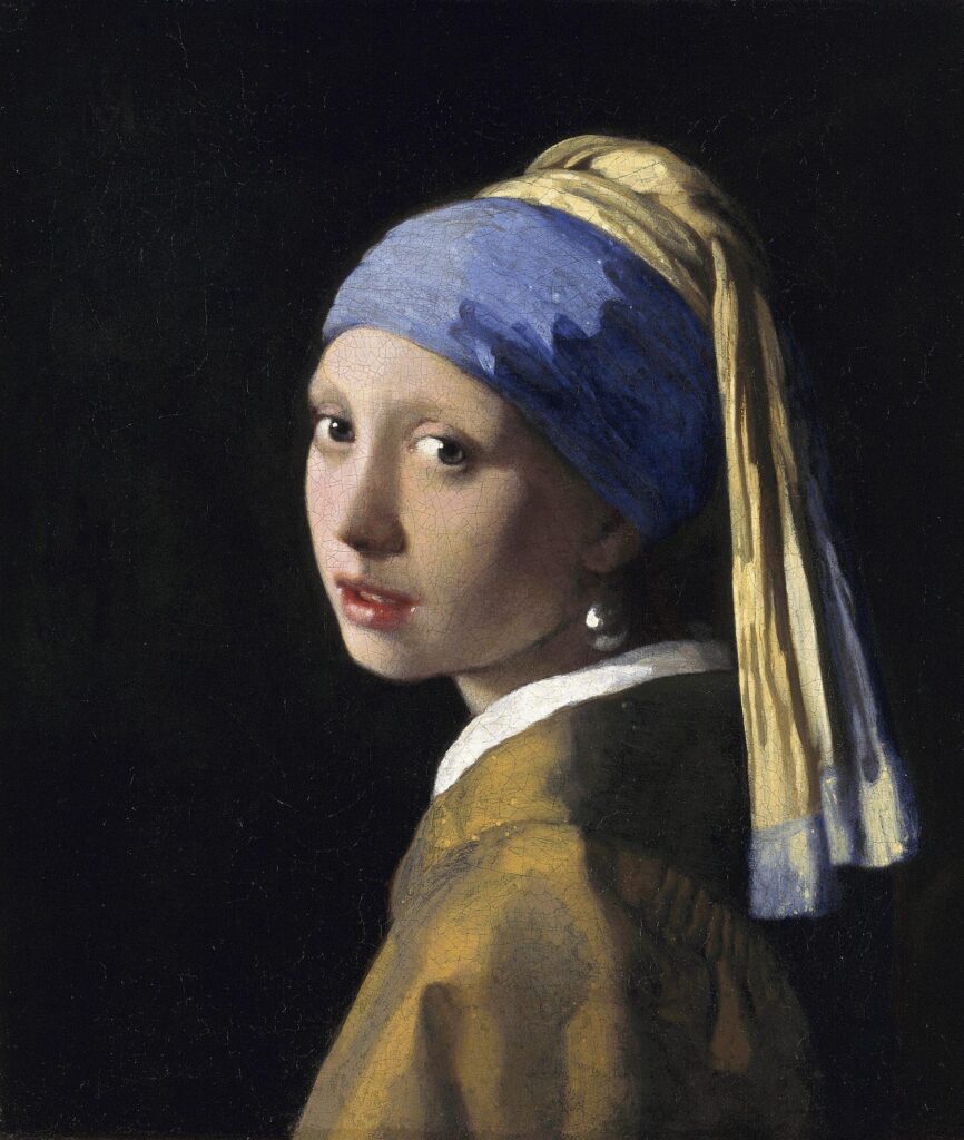 Portrait of a girl, at bust-length, facing left, looking at the viewer. She is wearing a yellow and blue turban, a light brown coat and an earring with a single pearl.