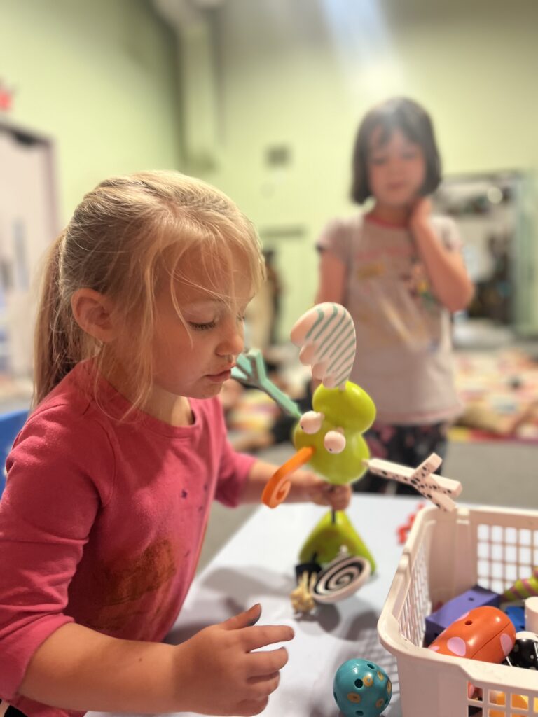 A young girl works on a sculpture while a second girl watches