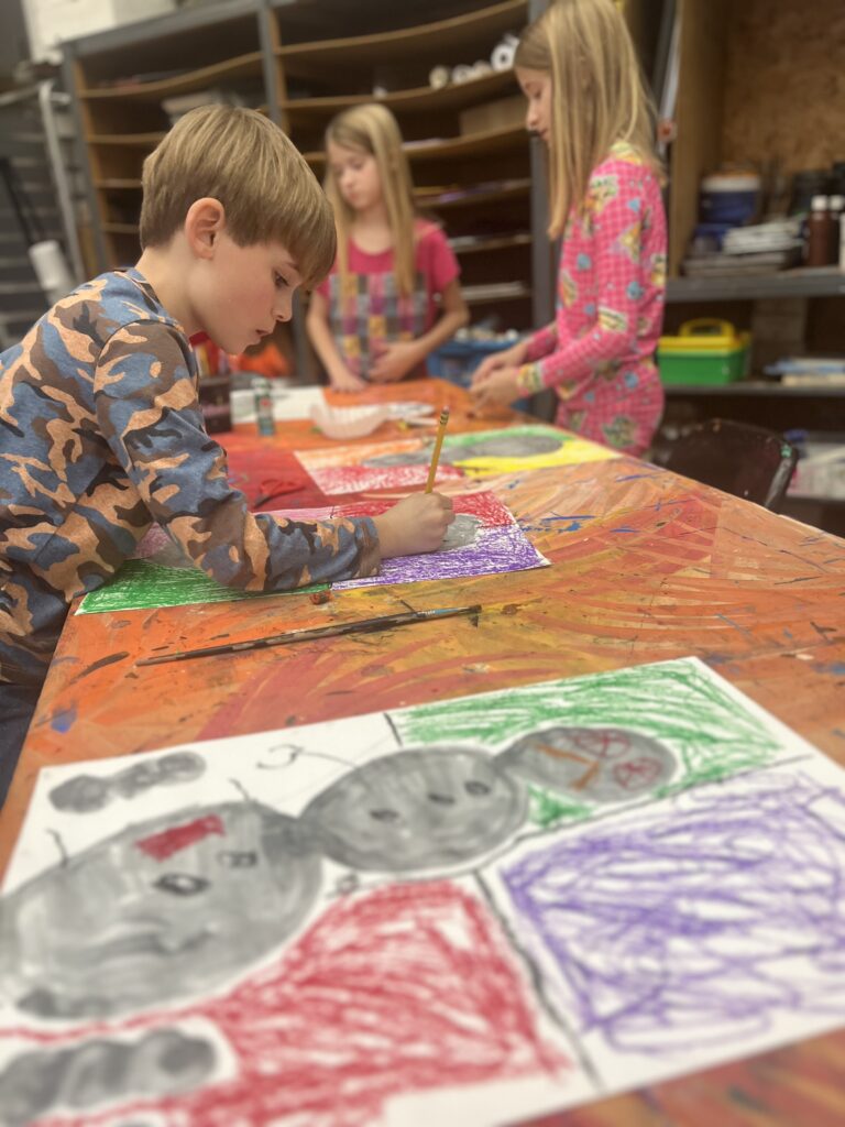 Boy draws snowman while two girls stand in background