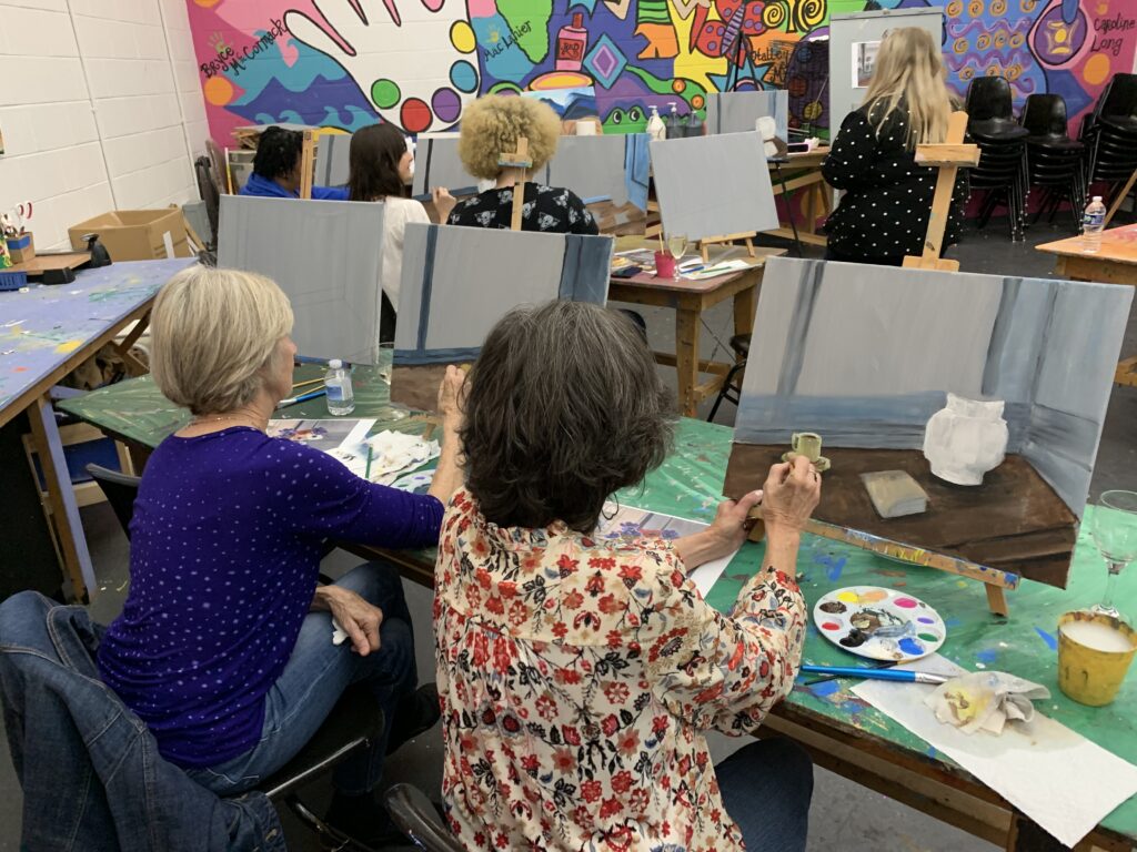 Participants in a painting class work on canvases