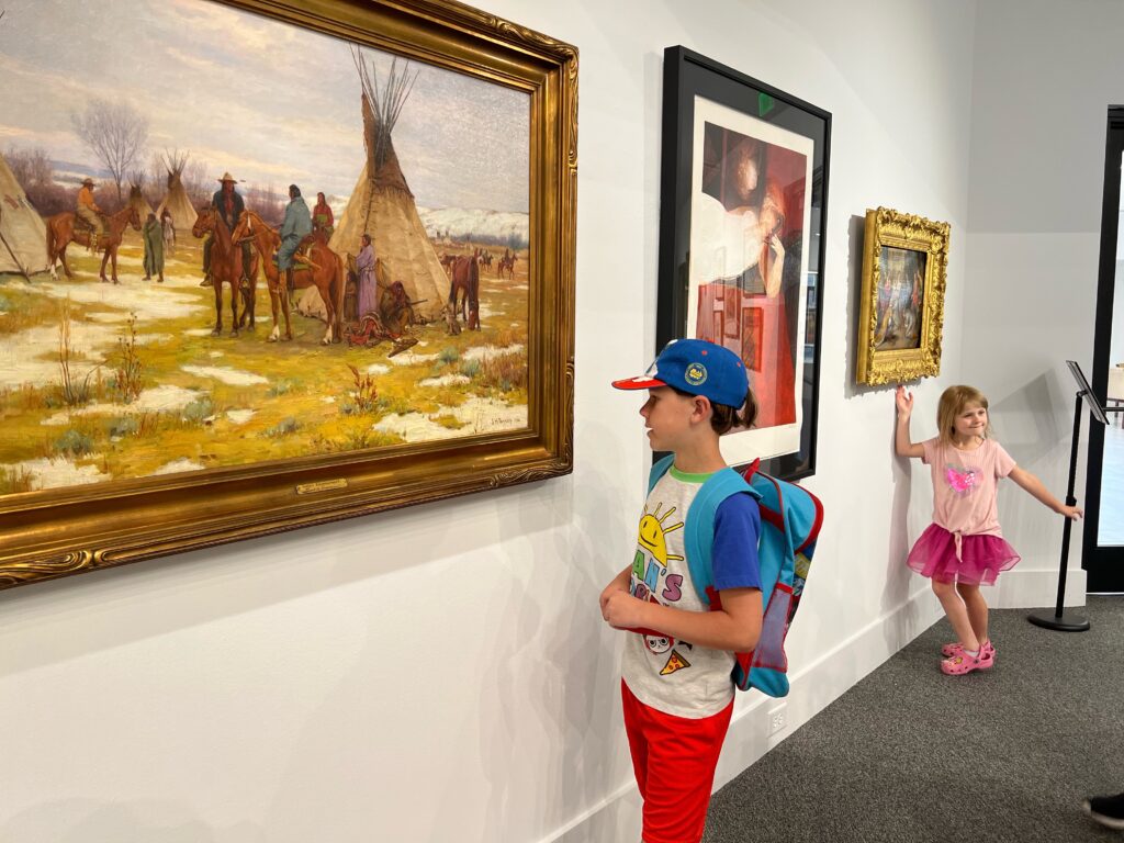 Boy looks at painting of Native Americans and girl stands in background