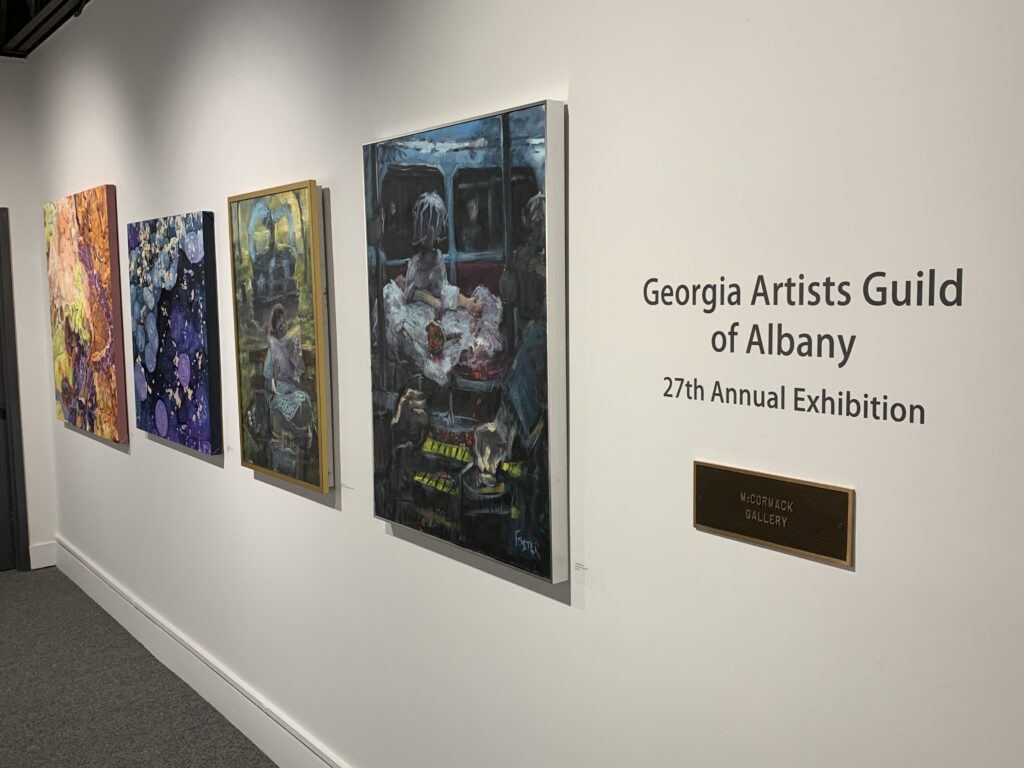 Three paintings on wall with show title