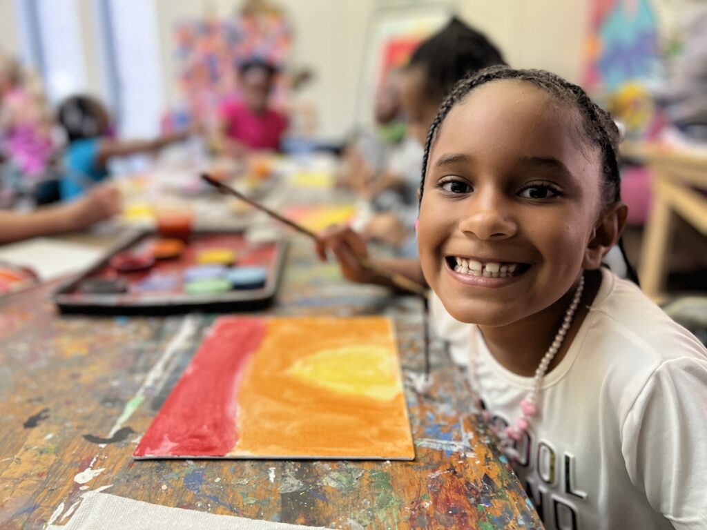 Girl smiles as she creates artwork at summer art camp