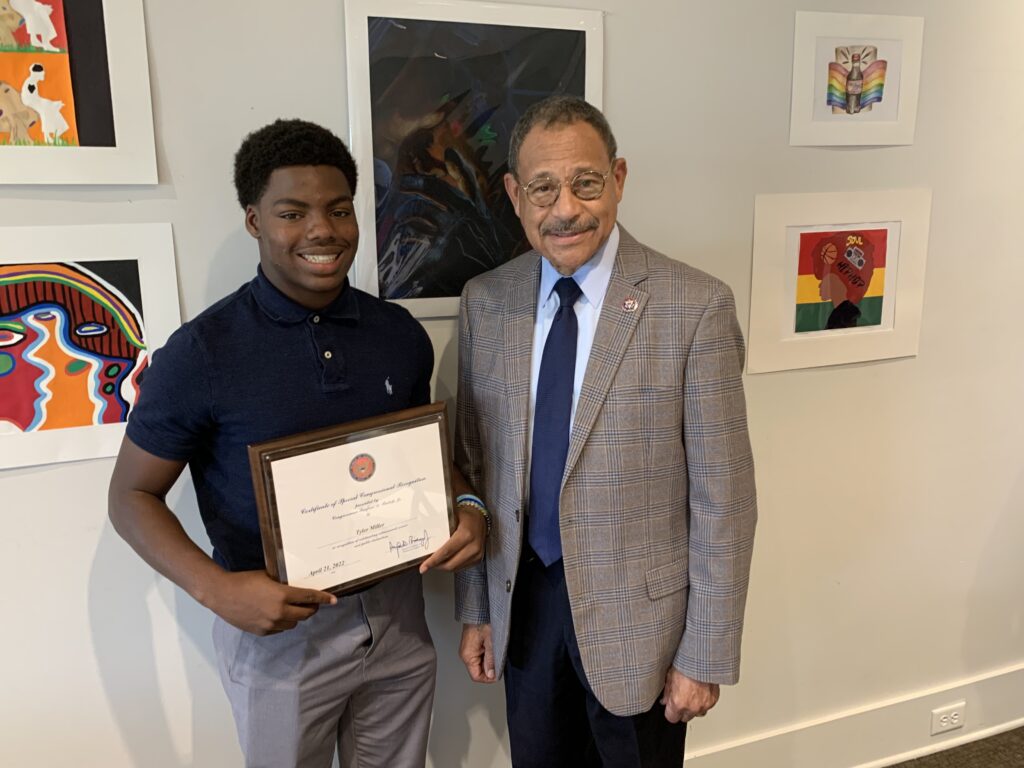 High school student and Congressman Bishop stand in front of the student's artwork. Student is holding a certificate.