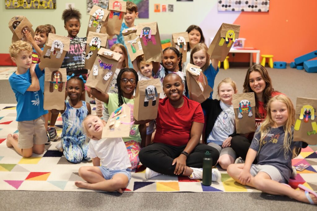 A group of Albany Museum of Art campers smile as they show off bag puppets they made.