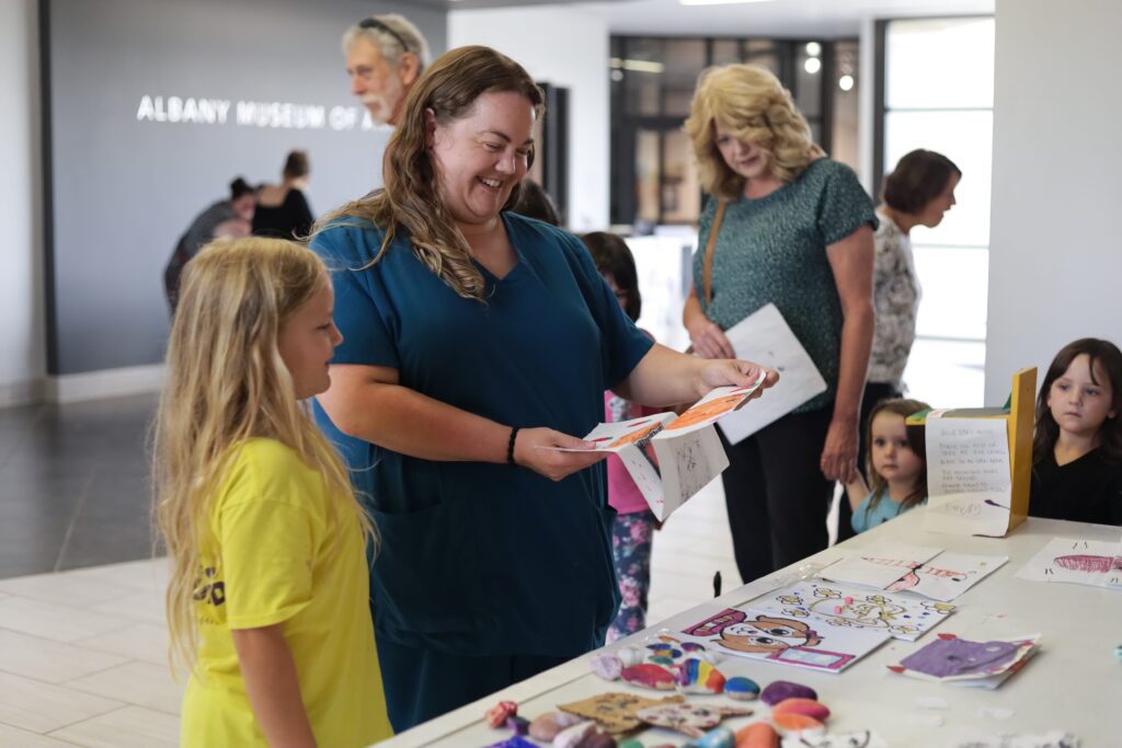 A child and two adults are seen looking at art created by campers