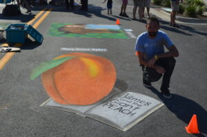 Chalk artist poses by his image of a giant peach and book