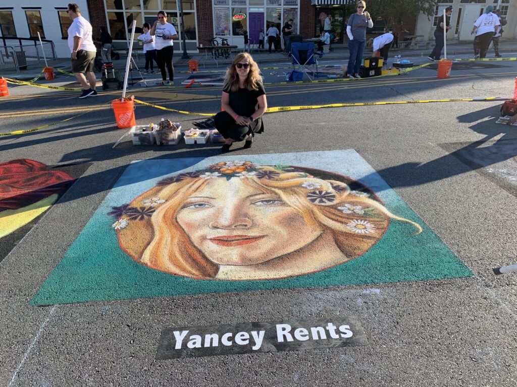 Artist poses with chalk art image of woman with flowers in her hair