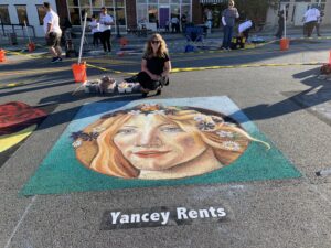 Artist poses with chalk art image of woman with flowers in her hair