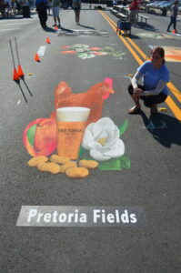 Artist poses with 3D chalk image of chicken, beer, peanuts and magnolia flower