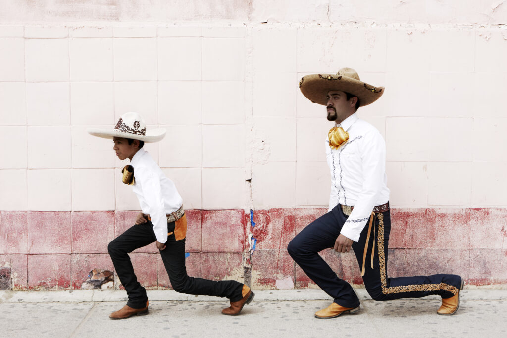 A boy and a man in white shirts and black pants and wearing sombreros pose