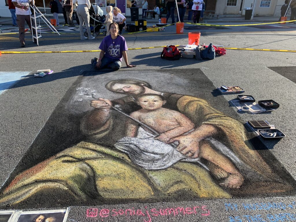 Artist poses with image of man holding baby and flowering branch